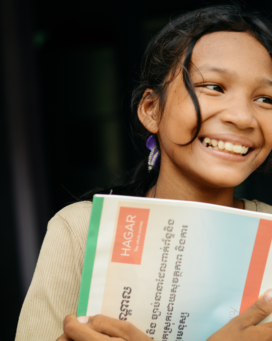 A smiling student holding a Hagar workbook